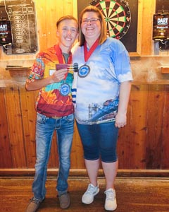 Photo of the two dart tournament champions from the 2022 Dart Tournament holding their medals standing in front of dart boards